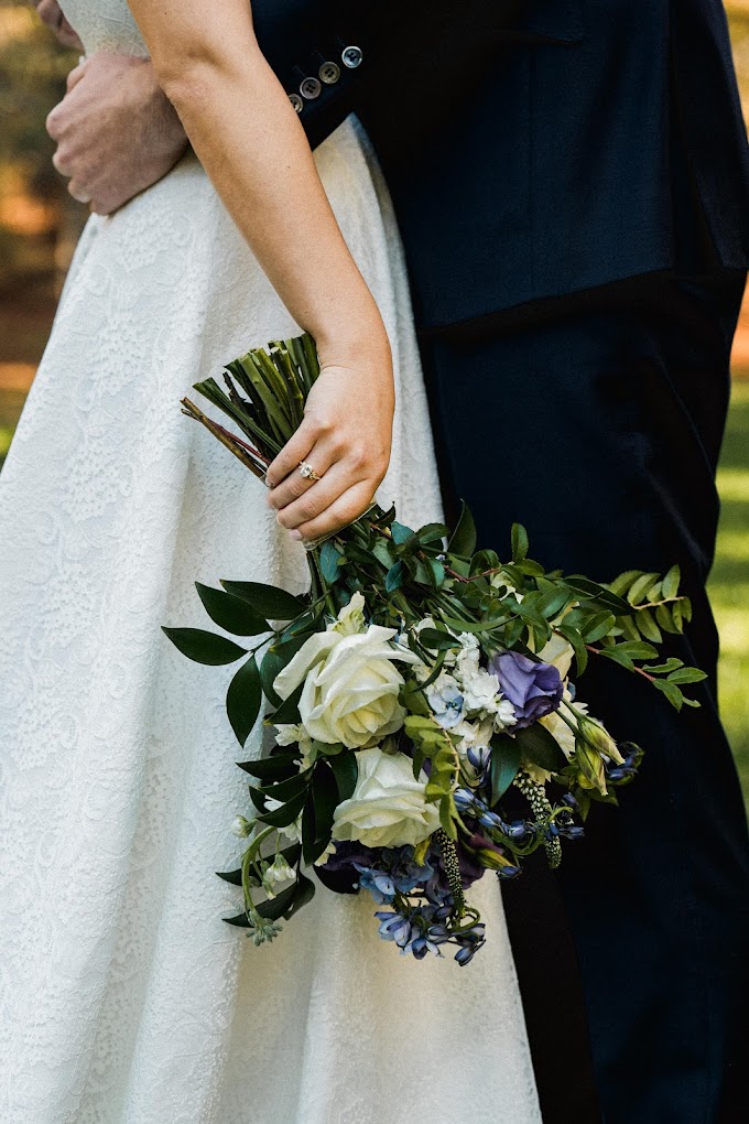 bride holding a bouquet at her side with her husband in frame